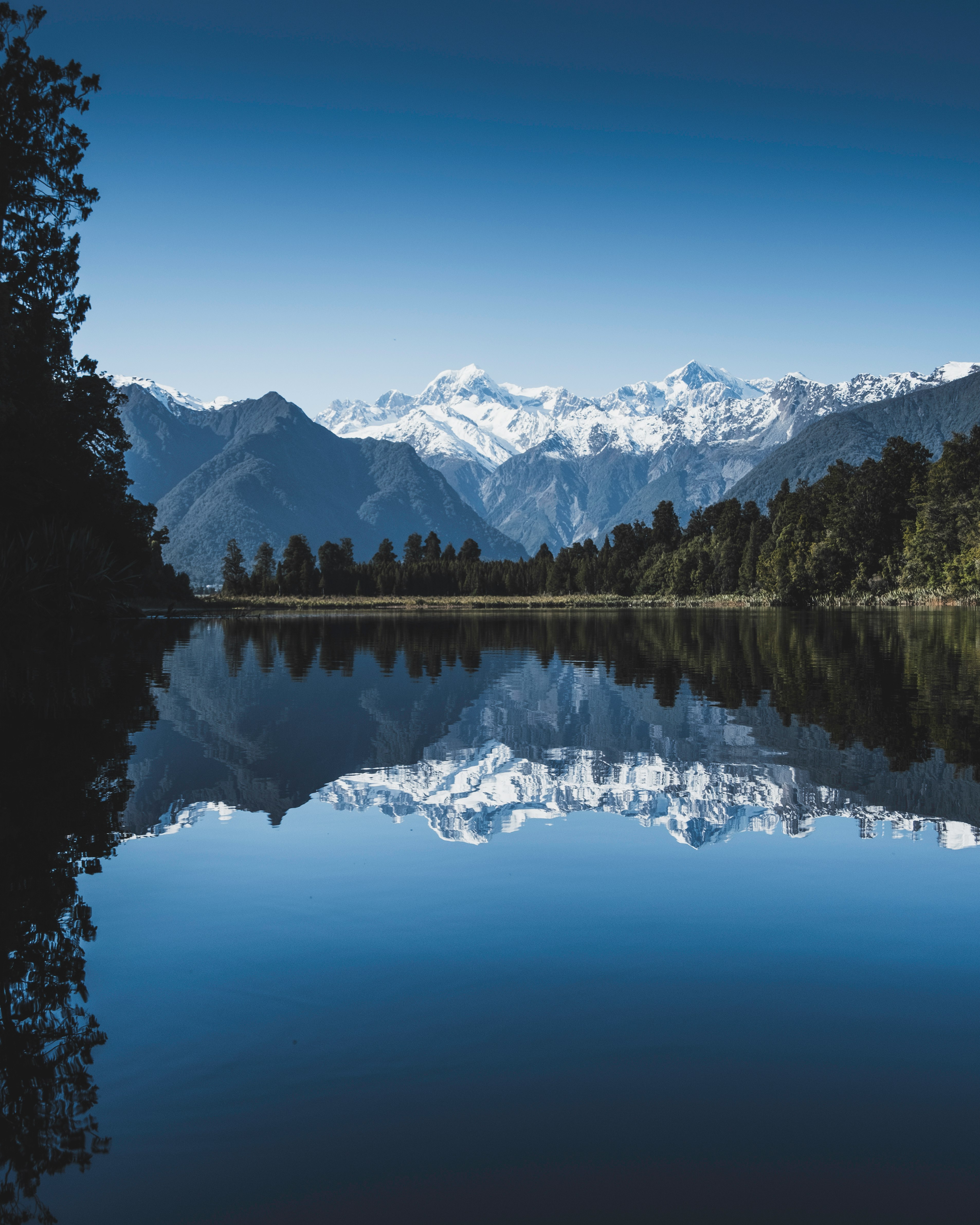 body of water between green trees under clear blue sky